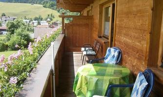 A balcony with wooden walls and a view of nature. Two chairs and a table are cozily set.