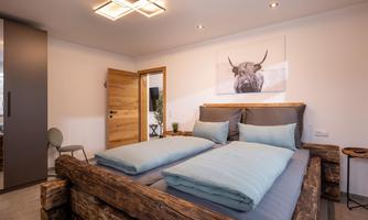 A modern bedroom with a large bed made of wood and gray bedding. A picture of an animal hangs on the wall, and the decor is simple and stylish.