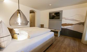 A modern bedroom with a large bed and a television on the wall. The warm lighting and stylish decor create a cozy atmosphere.