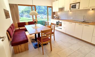 A modern kitchen with a dining table and chairs. Large windows offer a view of the surroundings.