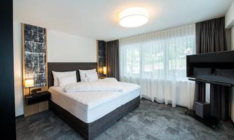 A modern bedroom with a large bed and bright curtains. The room has elegant furniture and plenty of daylight.