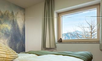 A cozy room with a bed and a window that offers a view of the mountains. The walls are decorated with a nature-inspired mural.