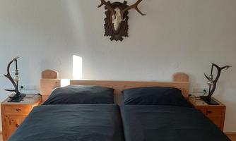 A bedroom with a double bed and black-covered mattresses. The walls are plain and a stylish lamp hangs above the bed.