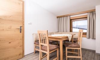 A cozy dining area with a wooden table and four chairs. A window with curtains and a wooden door are also visible.