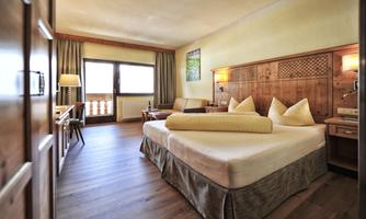 A cozy room with a large bed and wood details. Large windows provide plenty of light and a nice view outside.
