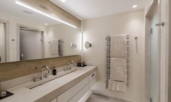 A modern bathroom with a double sink and large mirrors. White walls and soft lighting create a bright, inviting atmosphere.