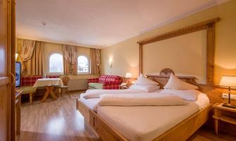 A cozy room with a large double bed and a wooden frame. There is bright light, warm colors, and a beautiful view through two windows.