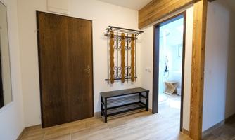 A bright entrance area with a wooden shelf and a dark brown door. To the right, a door leads into an adjoining room.