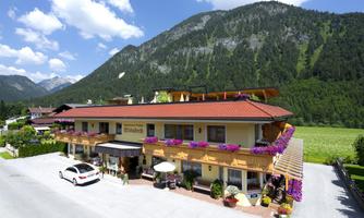 A charming hotel with blooming balcony plants in the mountains. The surroundings are green and picturesque, ideal for a relaxing stay.