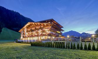 A charming mountain chalet with a illuminated facade in a picturesque landscape. Gentle hills and mountains are visible in the background.