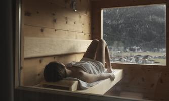 A person is relaxing in a wooden sauna with a view of the mountains. The atmosphere is calm and peaceful.