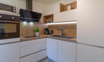 A modern kitchen with white furniture and a wooden countertop. It is well-equipped with appliances and has a stylish atmosphere.