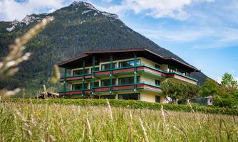 A modern building amidst a green meadow and in front of an impressive mountain panorama. The sky is clear and the surroundings are peaceful and inviting.
