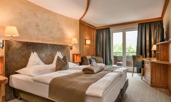 An elegant hotel room with a large double bed and modern furnishings. Large windows offer a view outside and provide pleasant light.