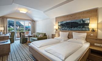 A cozy hotel room with a large double bed and stylish furnishings. The room offers a beautiful view of the mountains through large windows.