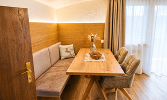 A cozy dining area with a wooden dining table and two chairs. The walls are in warm wood tones and the light is bright and friendly.