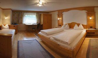 A cozy hotel room with two beds and an additional single bed. The decor is made of light wood and there is plenty of daylight.