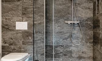 A modern bathroom with a shower and a toilet. The walls are in gray tiles and the design is simple and elegant.