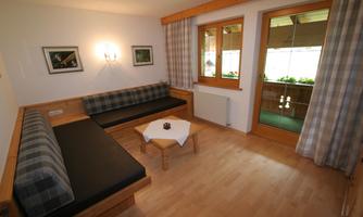 A bright living area with wooden furniture and cozy seating. Large windows provide plenty of light and a view of the greenery.