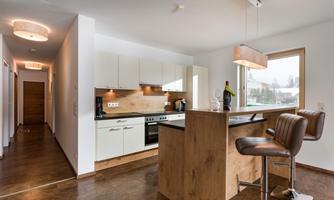 A modern kitchen with high-quality appliances and a wooden bar area. The room is bright and welcoming with large windows.