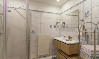 A modern bathroom with a shower, a sink, and wooden cabinets. The walls are decorated with white tiles and blue accents.
