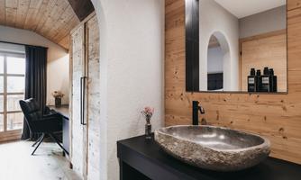 A modern bathroom with a sleek stone sink and wooden cladding. In the background, a mirror and stylish decor are visible.