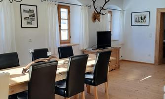 A cozy dining area with a large wooden table and black chairs. The room is bright and friendly with decorations on the walls.