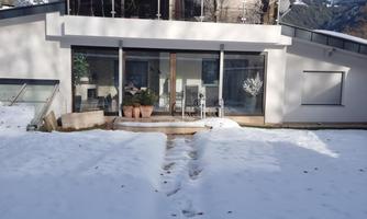 A modern house with large windows, surrounded by snow. The mountains can be seen in the background.