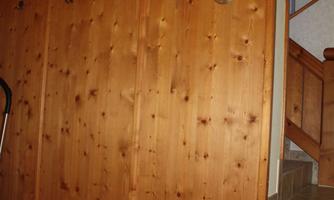 A wooden wall with hooks for jackets and a small carpet underneath. In the background, stairs can be seen leading upwards.