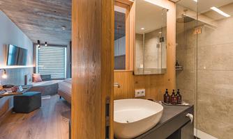 A modern bathroom with wood and tile design that features an elegant sink area. In the background, a cozy living space with a television and a sofa can be seen.