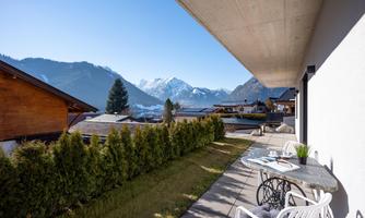 A terrace with a view of the mountains and the clear sky. Green lawn and modern furniture create a relaxed atmosphere.