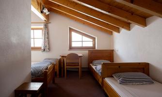 A simple room with slanted wooden ceilings. There are two single beds and a table in the middle.