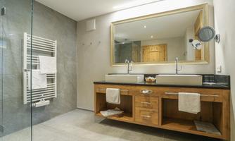 A modern bathroom with a large mirror surface and double sink. The walls are in neutral tones, and there is a stylish towel radiator.