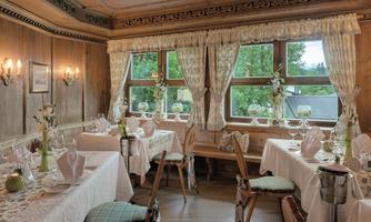 A cozy restaurant with wooden walls and elegant tables. Large windows provide plenty of natural light and a welcoming atmosphere.
