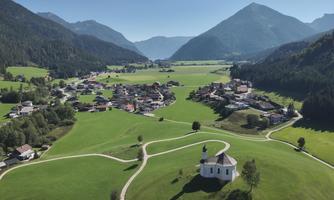 A picturesque landscape with green meadows and mountains in the background. In the foreground, there is a small church, surrounded by a gentle path.