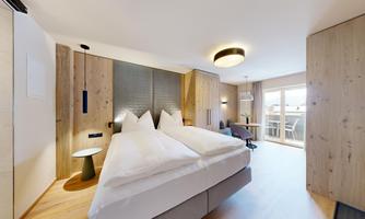 A modern hotel room with two beds, wood paneling, and large windows. The room is bright and inviting, with a minimalist design.
