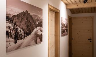 A modern hallway with wooden ceilings and doors. Black-and-white photos of mountains and snow hang on the wall.