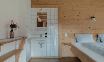 A cozy room with wooden paneling and a sink. There is a table with flowers and a double bed with checkered bedding.