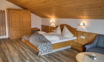A cozy room with wooden decor and a double bed. There is a table and a comfortable armchair as well as a wardrobe.