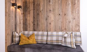 A modern living space with a gray couch and a decorative pillow. The wall is clad with wooden panels, and there is soft lighting.