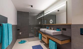 A modern bathroom with two sinks and a large mirror wall. Light blue towels and a stylish shower complete the appearance.