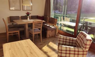 A cozy dining area with a wooden table and several chairs. Large windows offer a view of the surroundings and let in plenty of light.