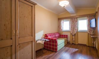 A cozy room with wooden cabinets and a sunny hue. There is a red sofa and a small table, as well as windows with curtains.