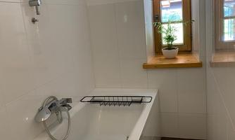 A modern bathroom with a bathtub and a small window. On the windowsill is a plant that brings life to the room.