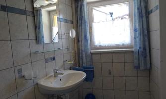 A simple bathroom with tiled walls and a sink. A window with curtains provides natural light.