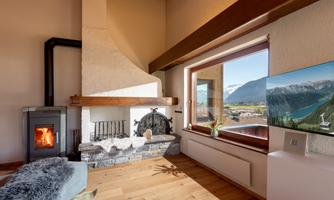 A cozy living room with a modern fireplace and a large window that offers a view of the mountains. The room is bright and inviting, with hardwood floors and contemporary furniture.
