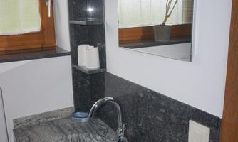 A modern bathroom with an elegant sink made of dark stone. In the background, a window with a plant is visible.