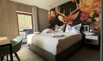 A modern bedroom with a large double bed and a striking wall decoration of a deer. By the window stands an elegant chair, and the room has a pleasant atmosphere.