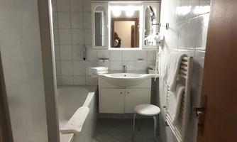 A modern bathroom with a bathtub, a sink, and a mirror. The walls are tiled and there is a shower cubicle.