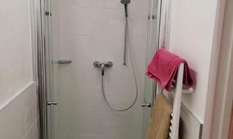 A modern shower with a glass partition and a showerhead. Towels in pink and beige are visible.